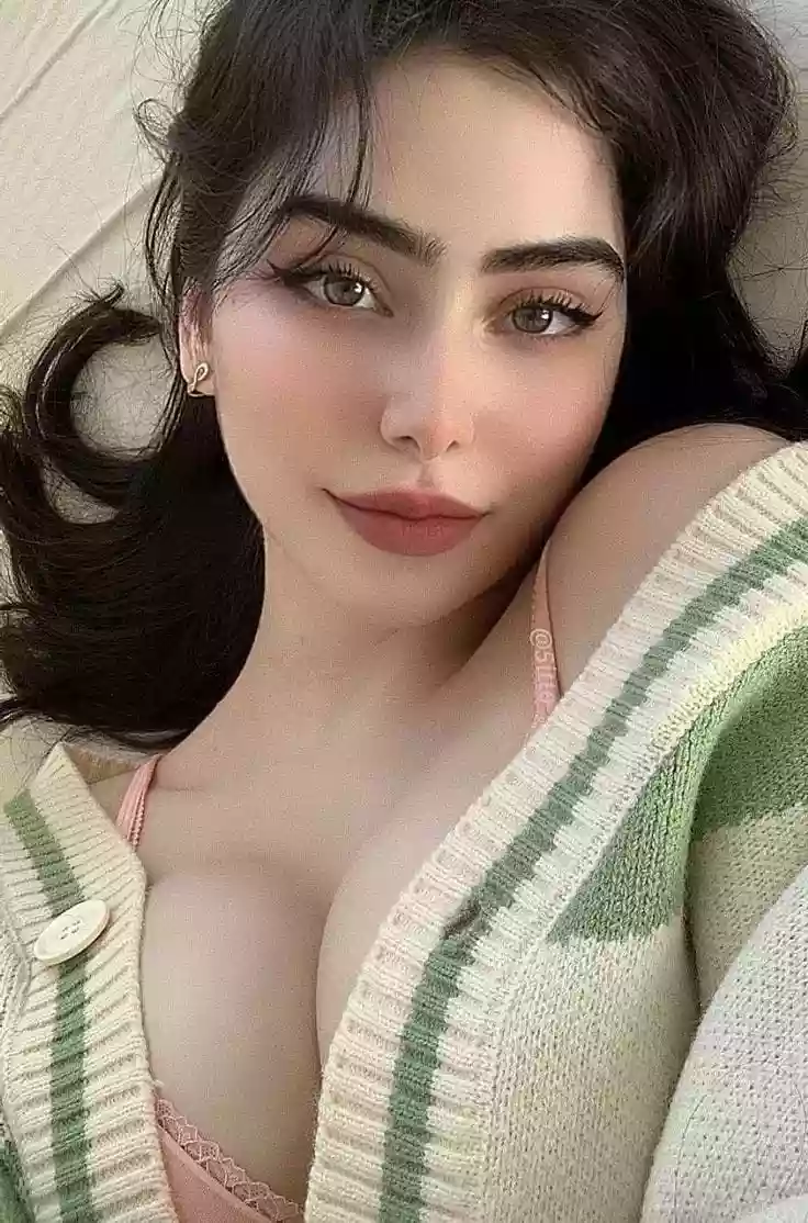 Close-up of a woman lying down, wearing a pink bra and a green striped cardigan, with subtle makeup and winged eyeliner.